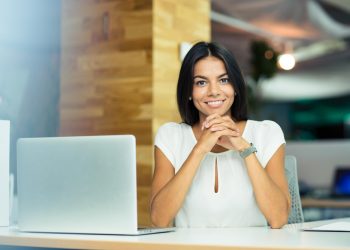 portrait-of-a-cheerful-business-woman-sitting-at-table-in-office portrait of cheerful business woman sitting in office