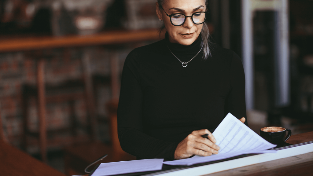 A woman wearing glasses sitting at a desk while reading documents