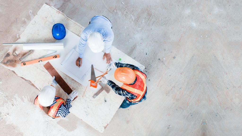 Overhead view of three individuals wearing hardhats around a desk looking at a blueprint