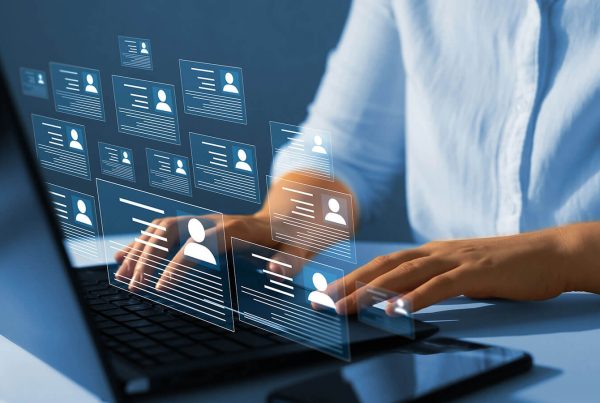 A close-up of an individual's hands typing at a laptop with icons popping up from the keyboard that resemble user profiles.