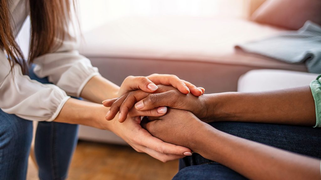 An image of two people holding hands supportively while sitting across from one another.