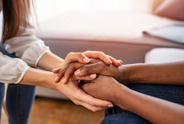 An image of two people holding hands supportively while sitting across from one another.