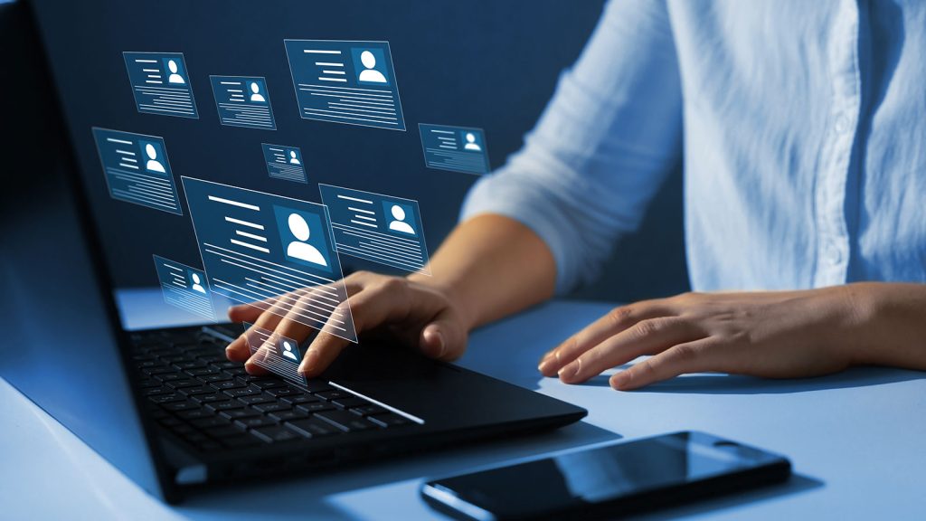 Hands typing on a laptop on a desk with icons of people floating above.