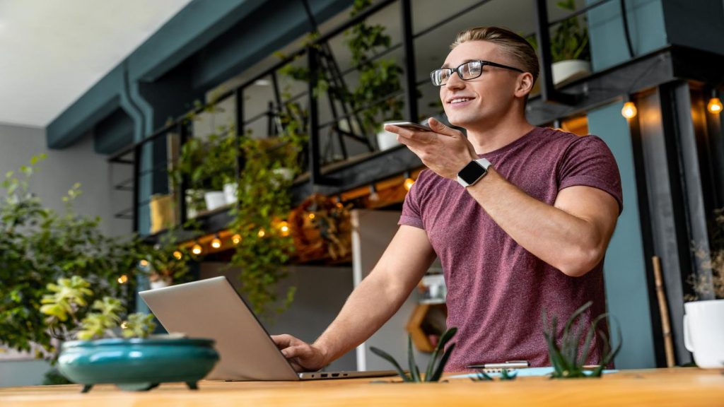 Male speaks on his cell phone with a laptop in front of him, looking positive and professional