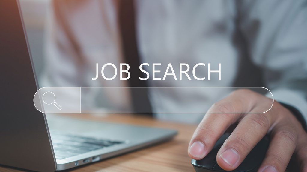 A close up of a man sitting at a desk with a laptop open and his hand using the computer mouse with the words 'Job Search' over the image.