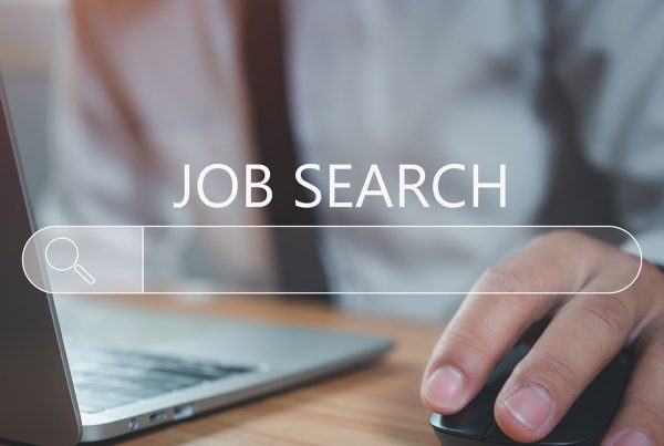 A close up of a man sitting at a desk with a laptop open and his hand using the computer mouse with the words 'Job Search' over the image.