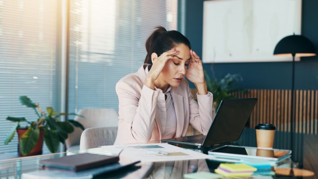 A women sitting at a desk with a laptop with her hands on her head looking frustrated