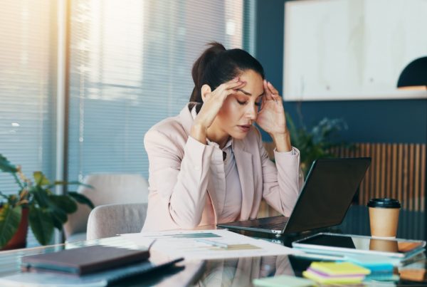 A women sitting at a desk with a laptop with her hands on her head looking frustrated