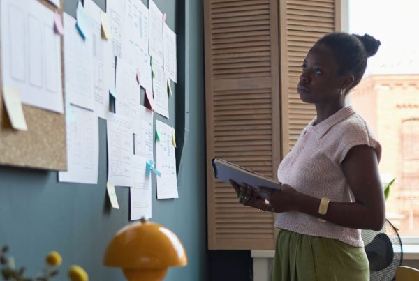 A woman in professional attire standing in her office looking at a corkboard filled with papers