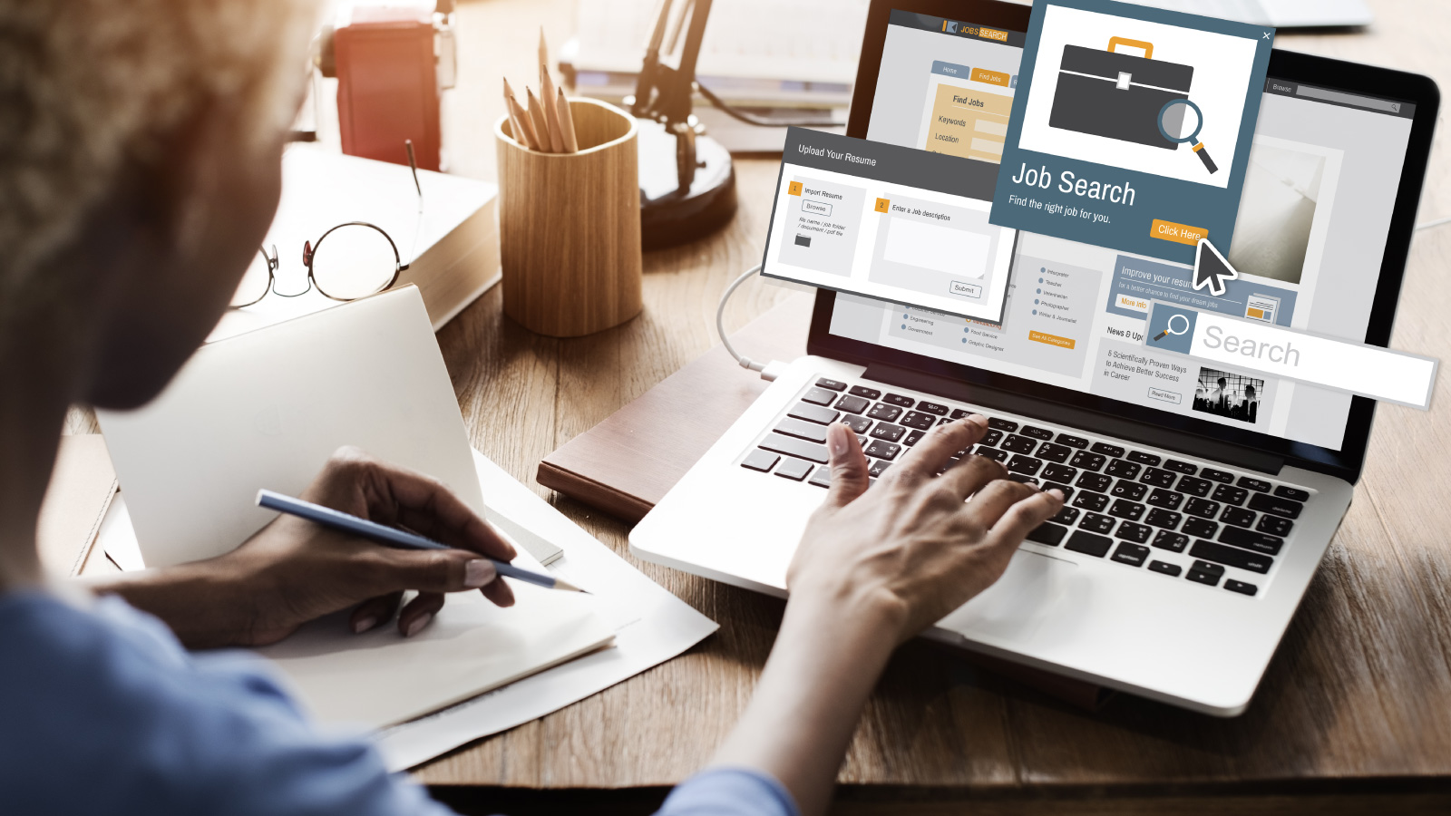 A woman sitting at a desk typing on a laptop with a notebook next to her. On the laptop screen it has an icon that says 'job search'