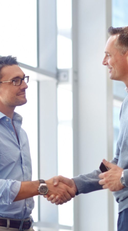 Two men wearing professional attire shaking hands in an office