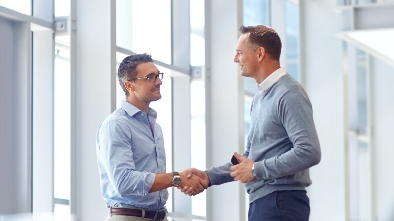 Two men wearing professional attire shaking hands in an office