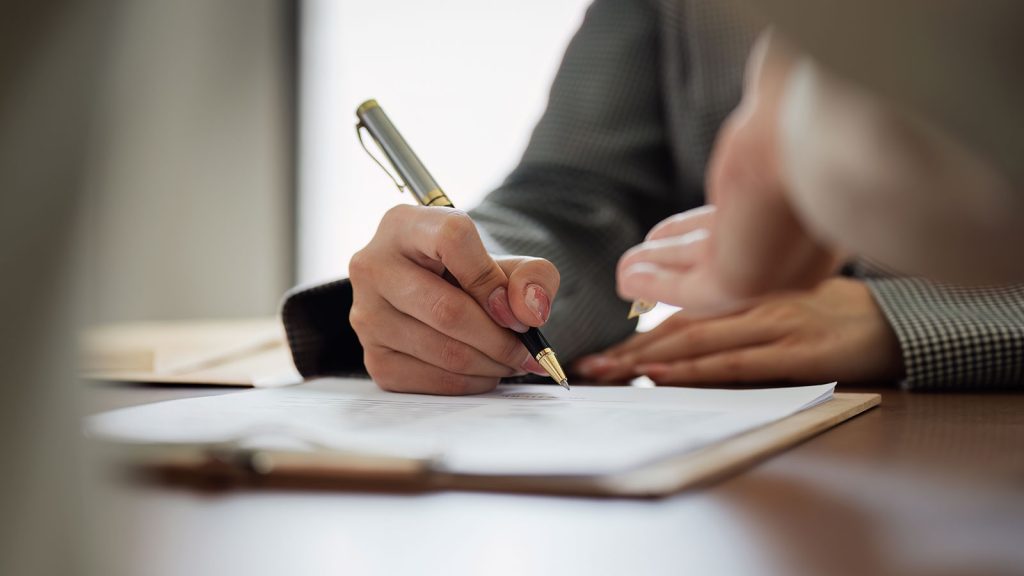 A hand holding a pen while writing on a document