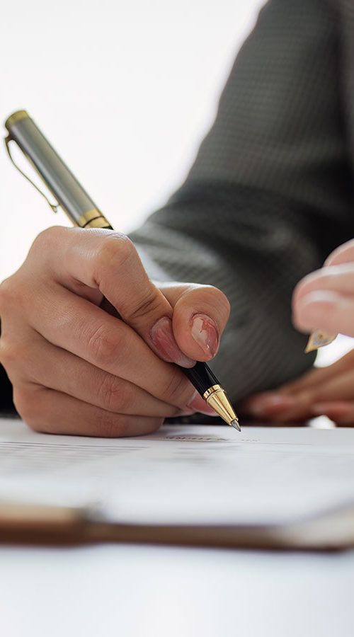 A hand holding a pen while writing on a document