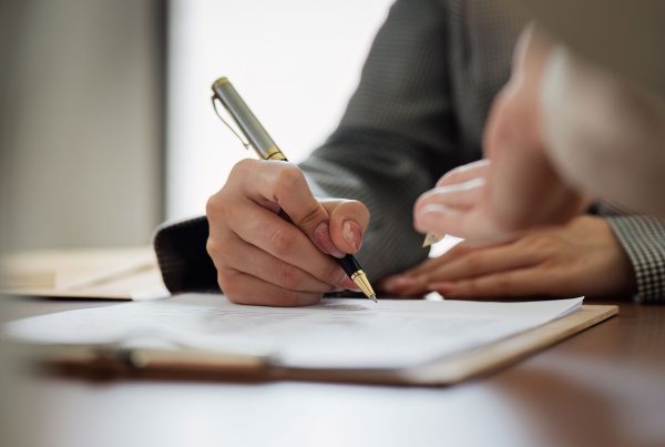 A hand holding a pen while writing on a document
