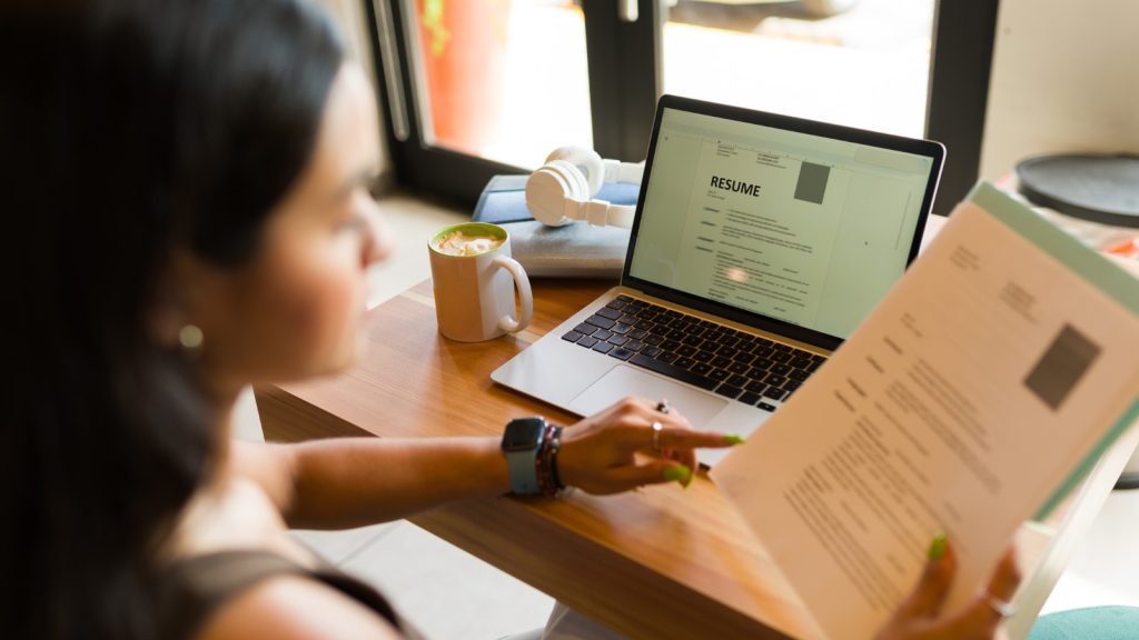 A women sitting at a desk with a laptop holding a resume in her hand