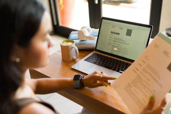 A women sitting at a desk with a laptop holding a resume in her hand