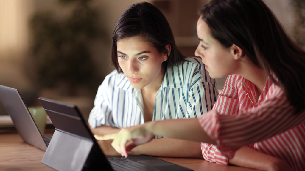 two women in business attire looking at a tablet with one pointing to the screen