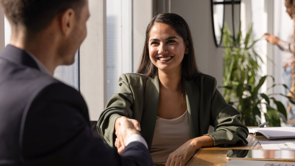 A woman in professional attire shaking the hand of a man in a suit