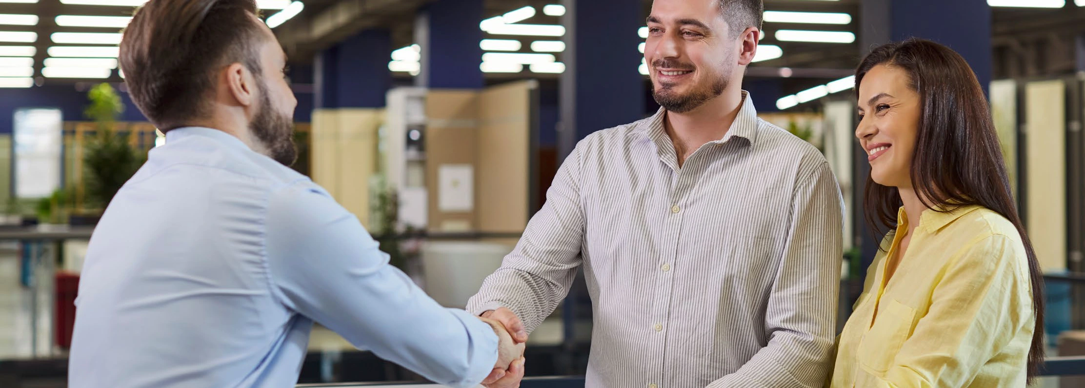 Two professionals shaking hands as a colleague looks on in an office
