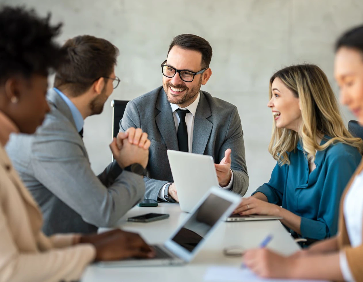 A team in conversation around a conference table with laptops and tablets