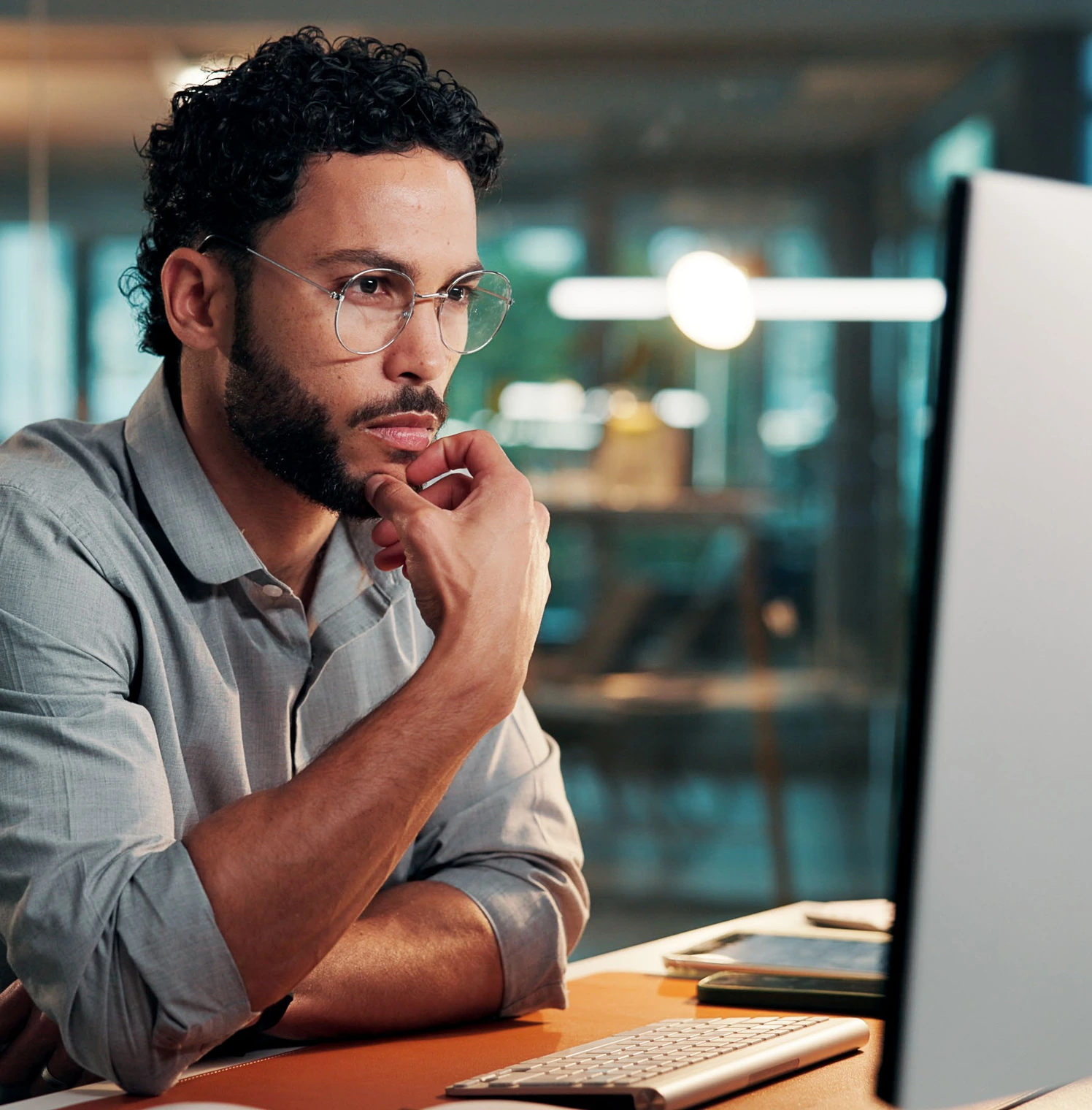 A developer in glasses studying a computer screen at an office desk