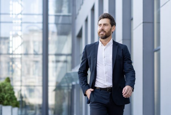 A man wearing a suit walking outside next to a commercial building