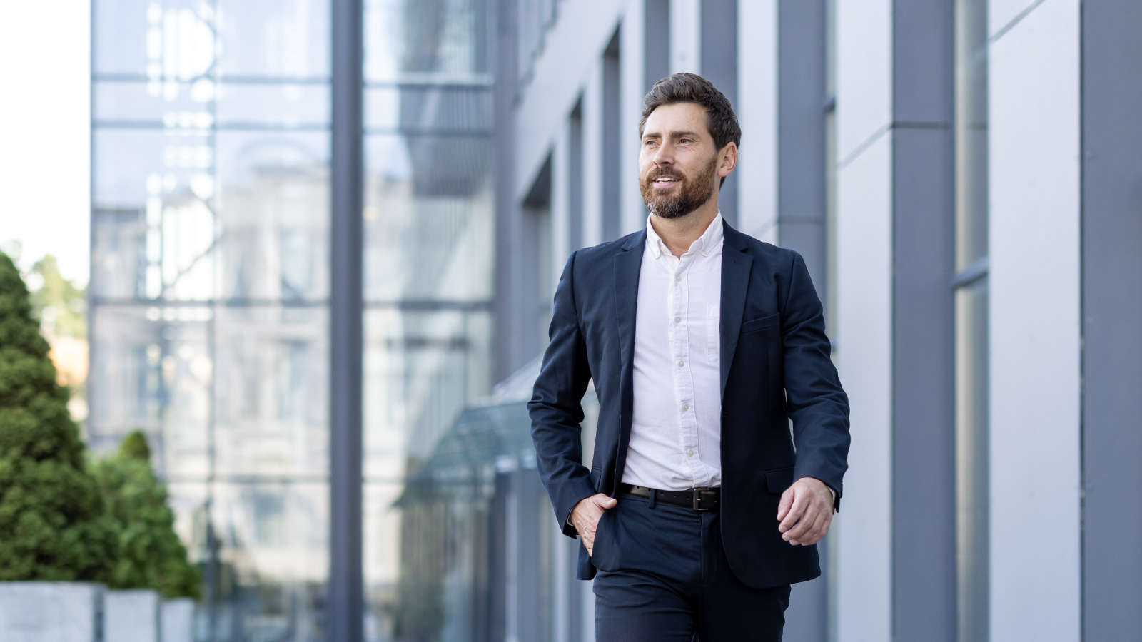 A man wearing a suit walking outside next to a commercial building